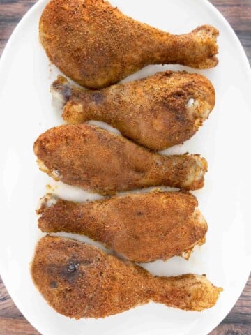 Seasoned smoked chicken legs on a white platter.
