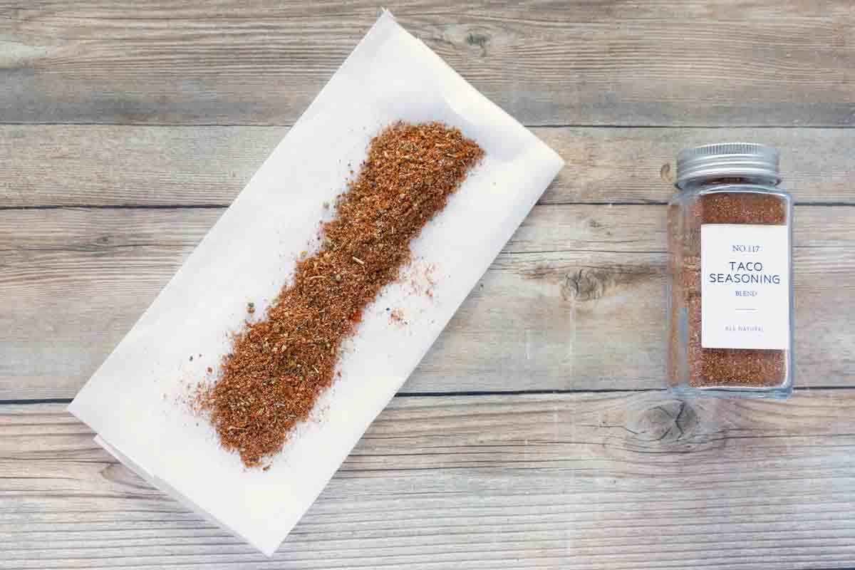 taco seasoning on white paper next to bottle of seasoning.