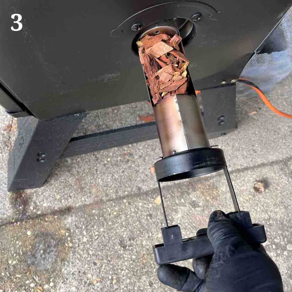 gloved hand putting wood chips into the smoker.