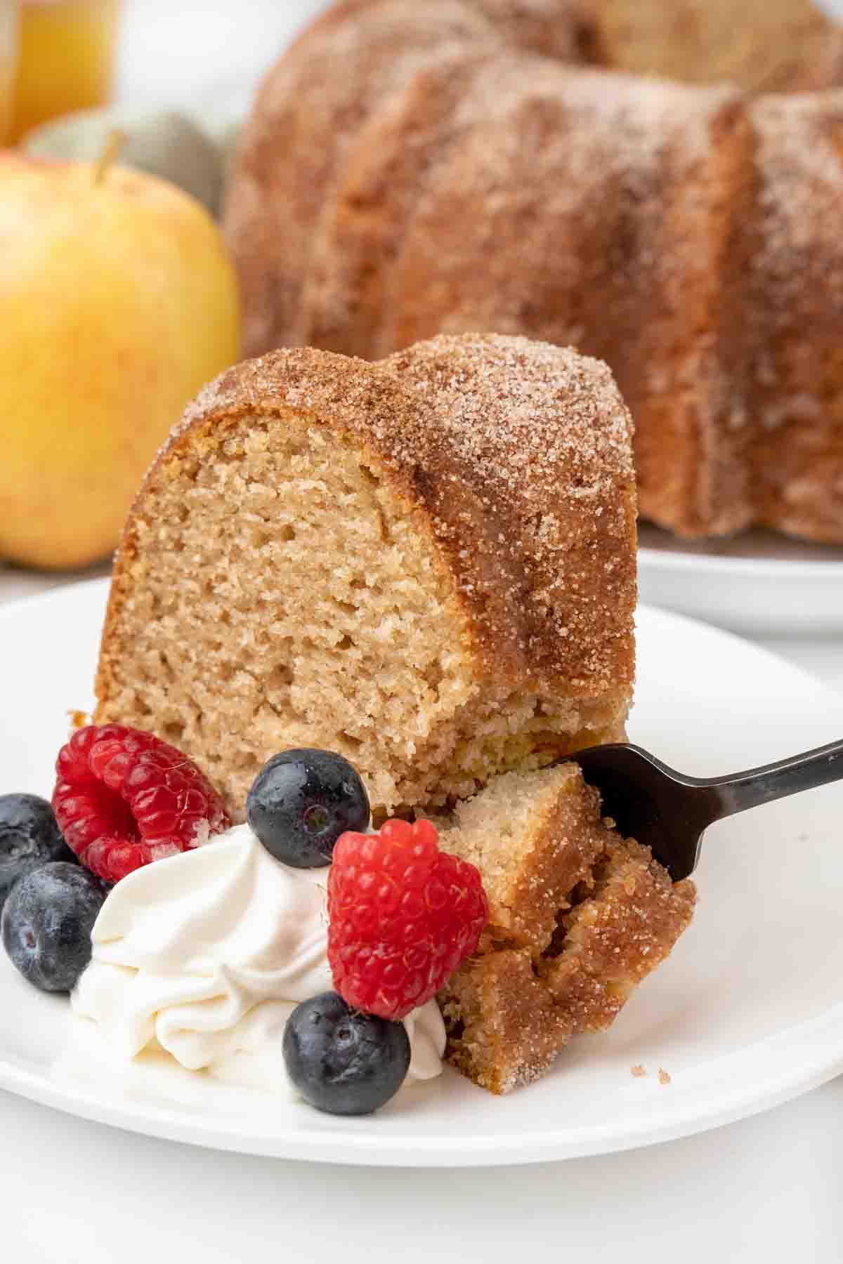 Apple cider bundt cake with whipped cream and berries on a white plate.