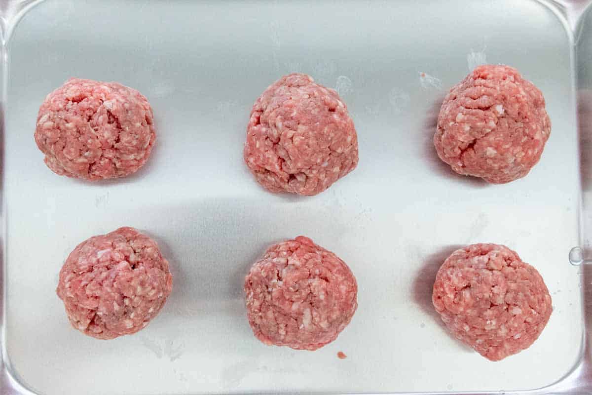 ground meat rolled into balls sitting on small sheet pan.