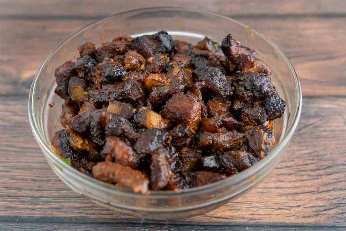 Smoked pork belly burnt ends with barbecue sauce in a glass bowl.