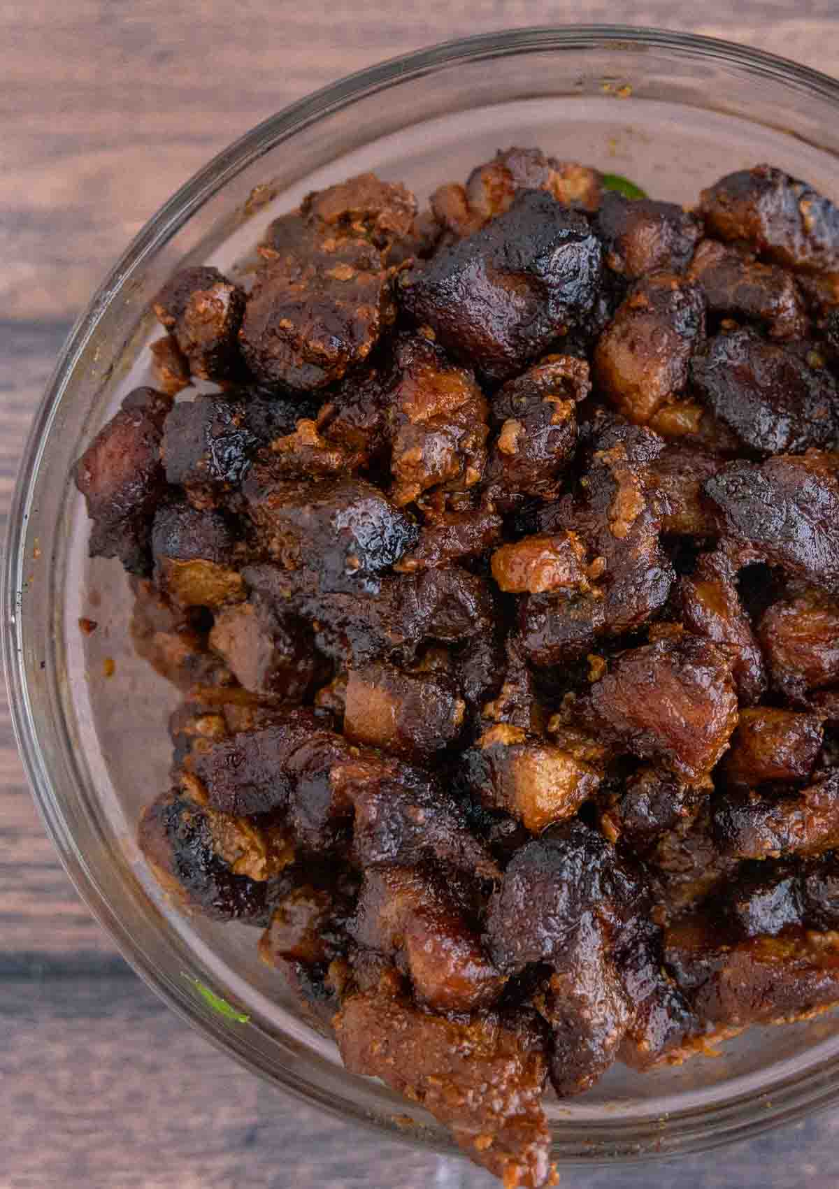 smoked pork belly burnt ends with barbecue sauce in a glass bowl.