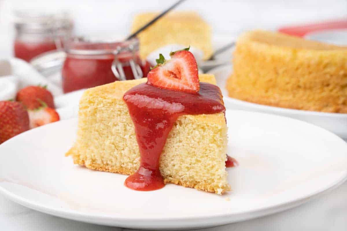 Slice of sponge cake with strawberry coulis on a white plate.