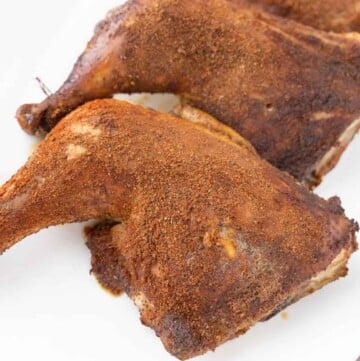 smoked chicken leg quarters on a white platter.