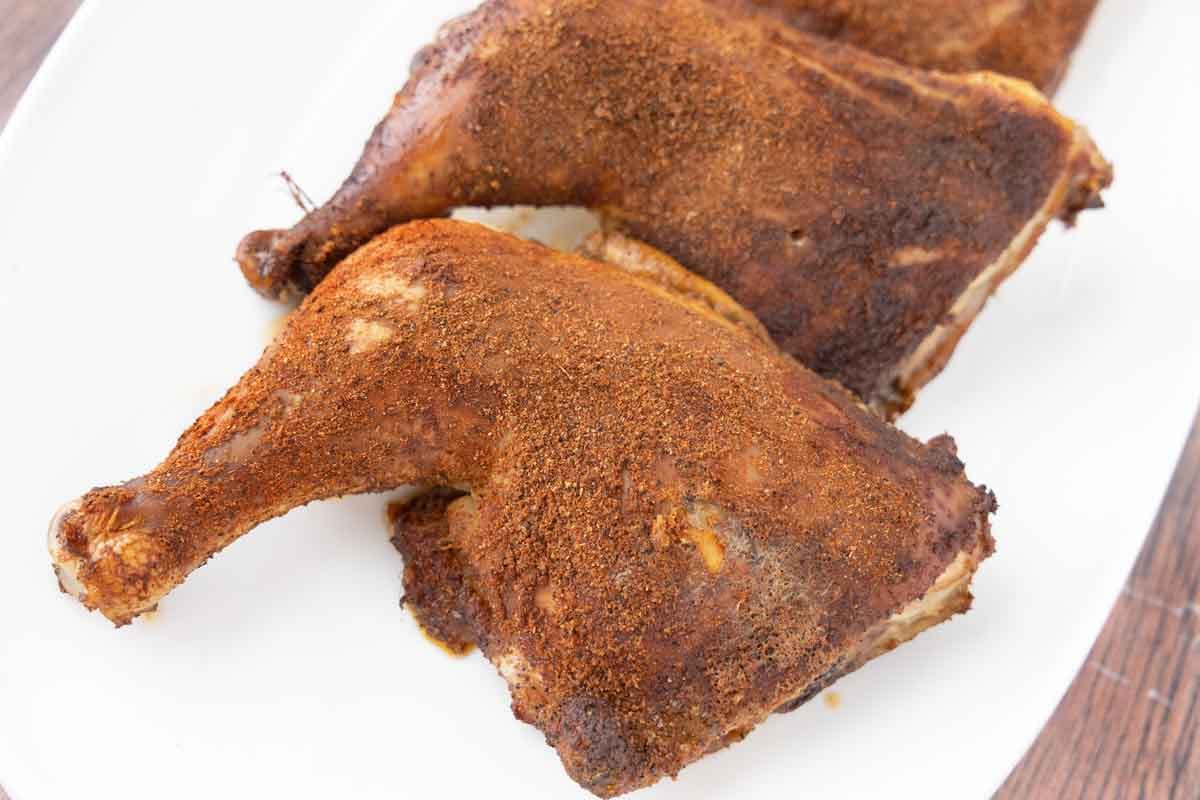 smoked chicken leg quarters on a white platter.