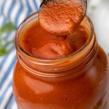 Ball jar of enchilada sauce with a spoonful being taken out of the jar.