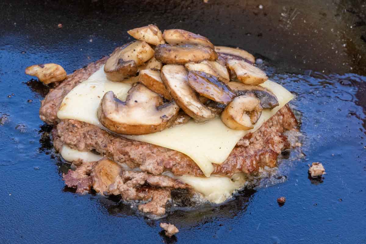 mushroom Swiss smash burgers stacked on the grill.