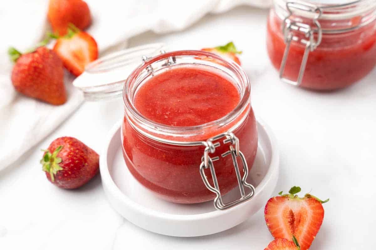Strawberry coulis in a a jar on a white plate.