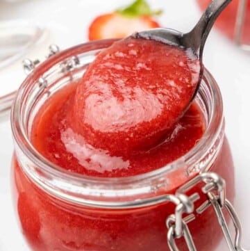 Strawberry coulis in a a jar with a spoon coming out of the jar.