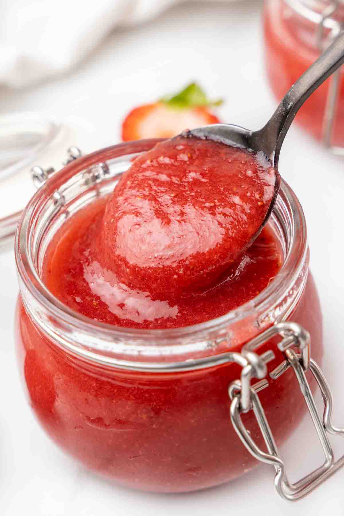 Strawberry coulis in a a jar with a spoon coming out of the jar.