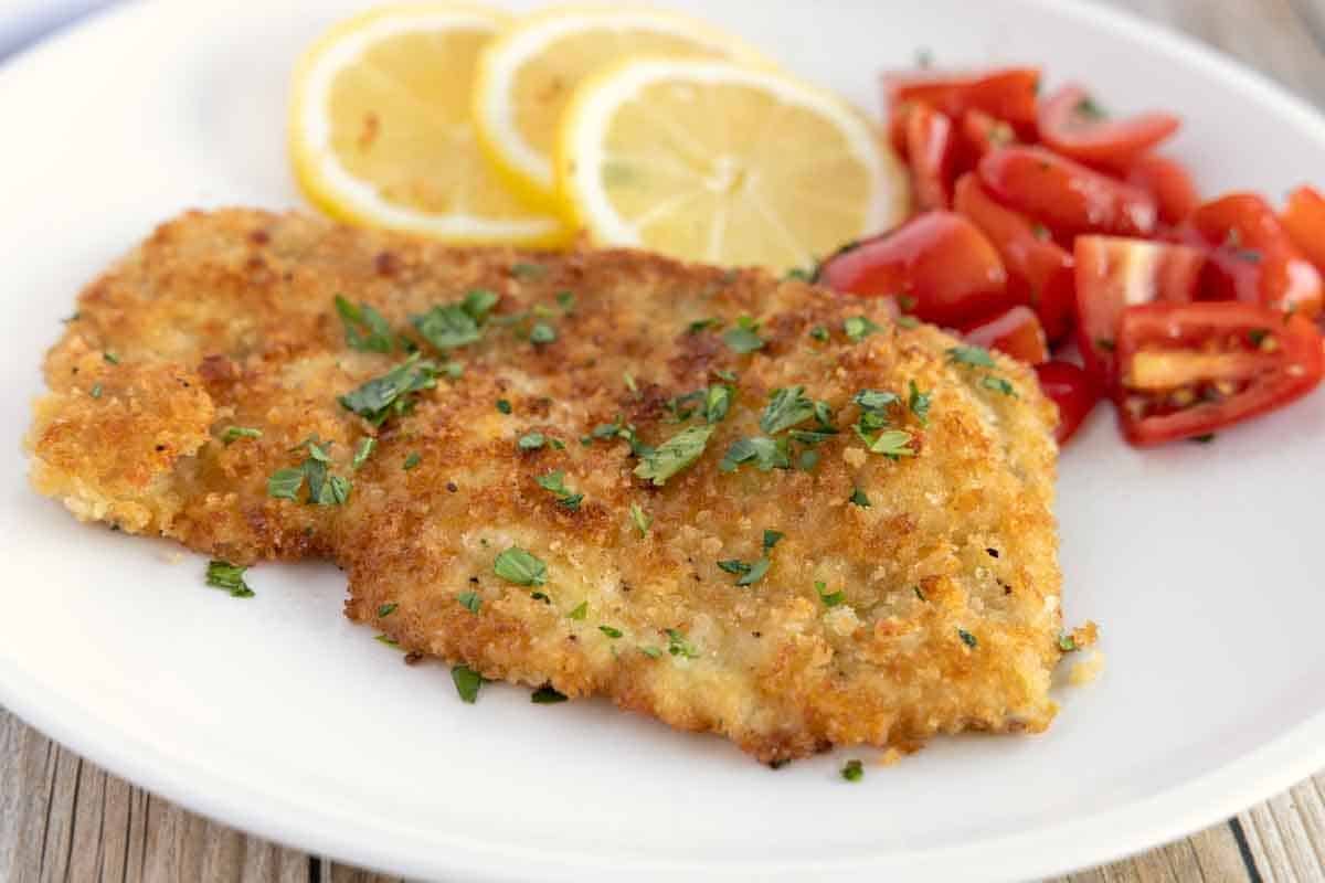 Wiener Schnitzel (veal schnitzel) on a white plate with lemon circles and tomatoes.