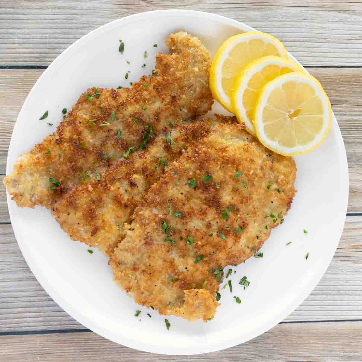 Wiener Schnitzel (veal schnitzel) on a white plate with lemon circles.