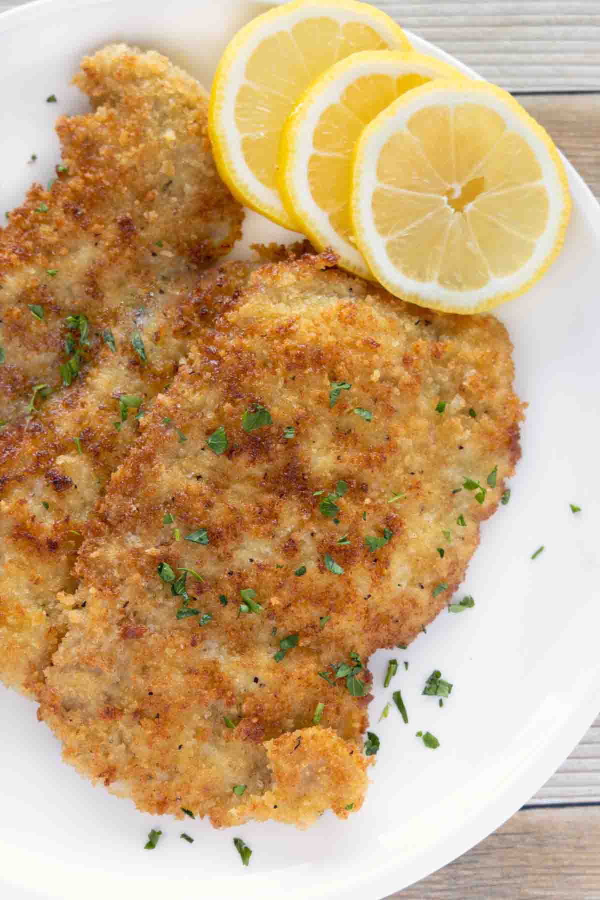 Wiener Schnitzel (veal schnitzel) on a white plate with lemon circles.