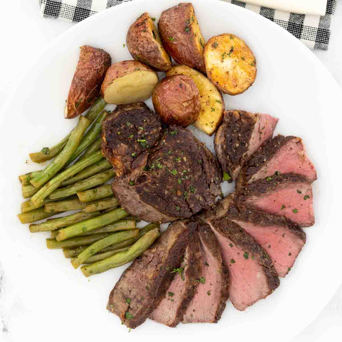 Sliced pan seared filet mignon on a white plate with potatoes and green beans.