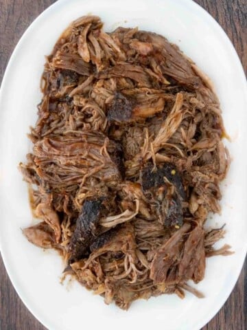 bbq smoked pulled pork butt on a white platter.