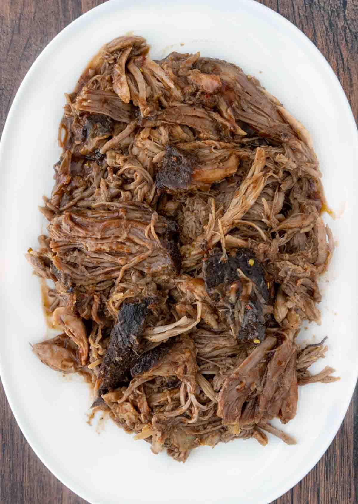 bbq smoked pulled pork butt on a white platter.