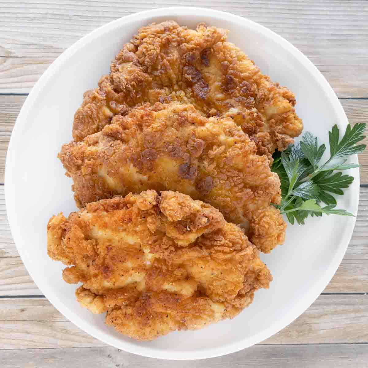 Three pieces of Chicken fried chicken on a white plate.
