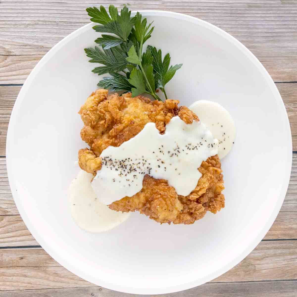 Chicken fried chicken with country gravy on a white plate.