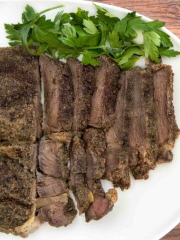 Sliced smoked chuck roast on a white platter with parsley sprigs.