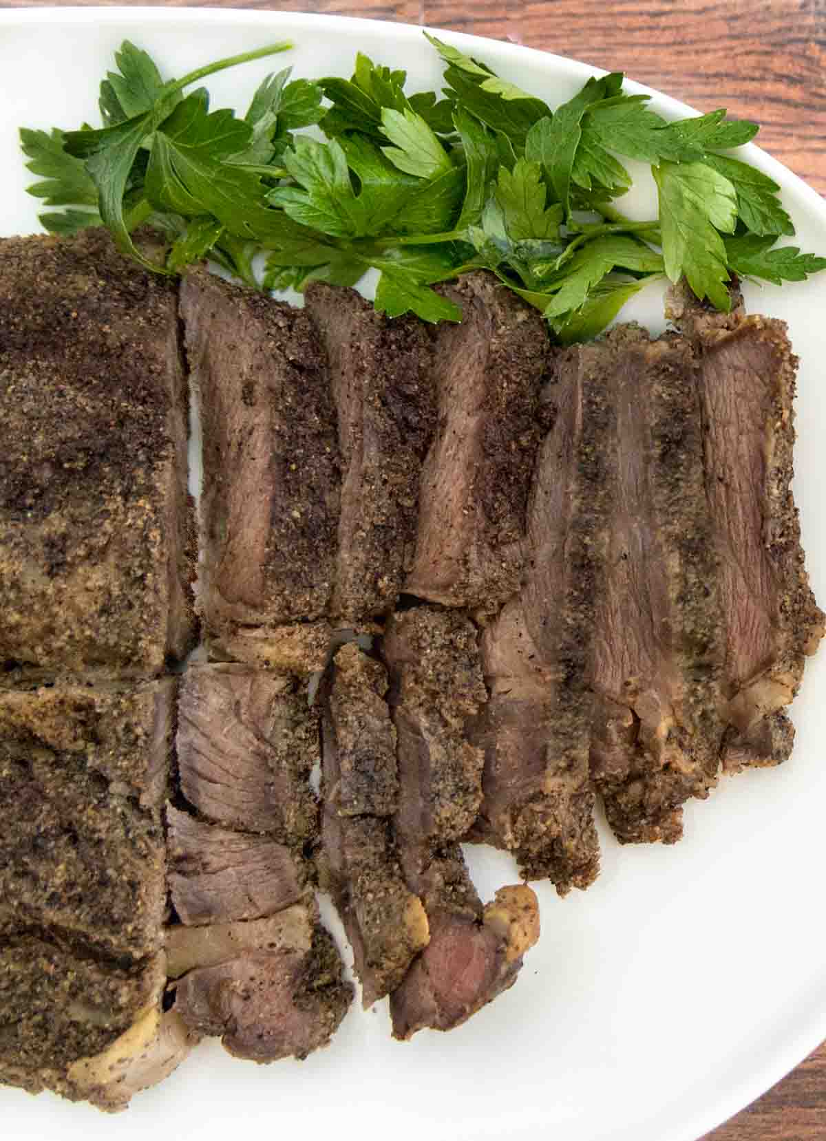 Sliced smoked chuck roast on a white platter with parsley sprigs.