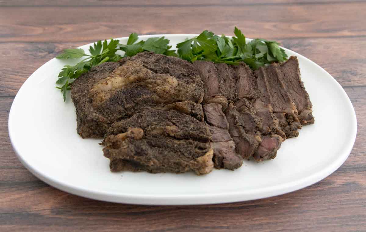 Smoked chuck roast on a white platter with parsley sprigs.