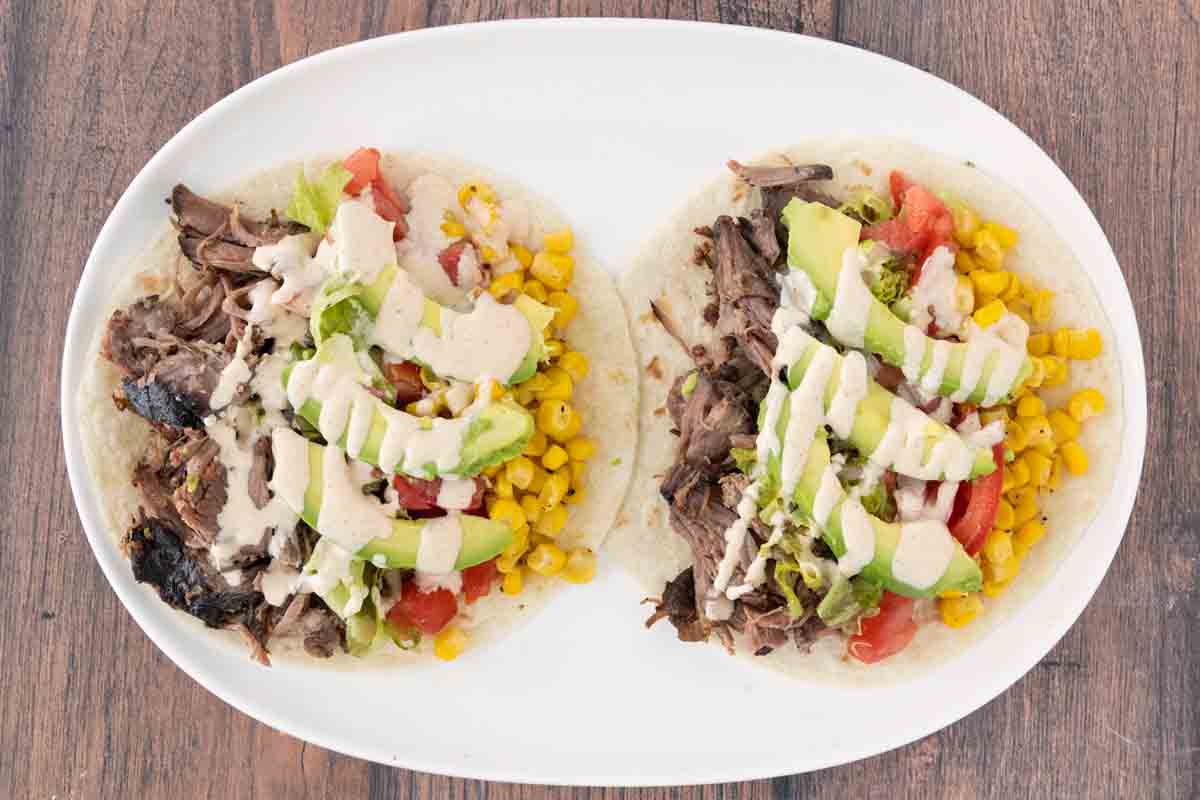 Two smoked chuck roast tacos on a white platter.
