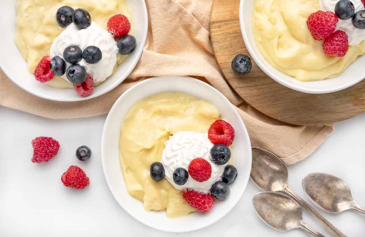 Vanilla custard in a white bowl topped with whipped cream and berries.