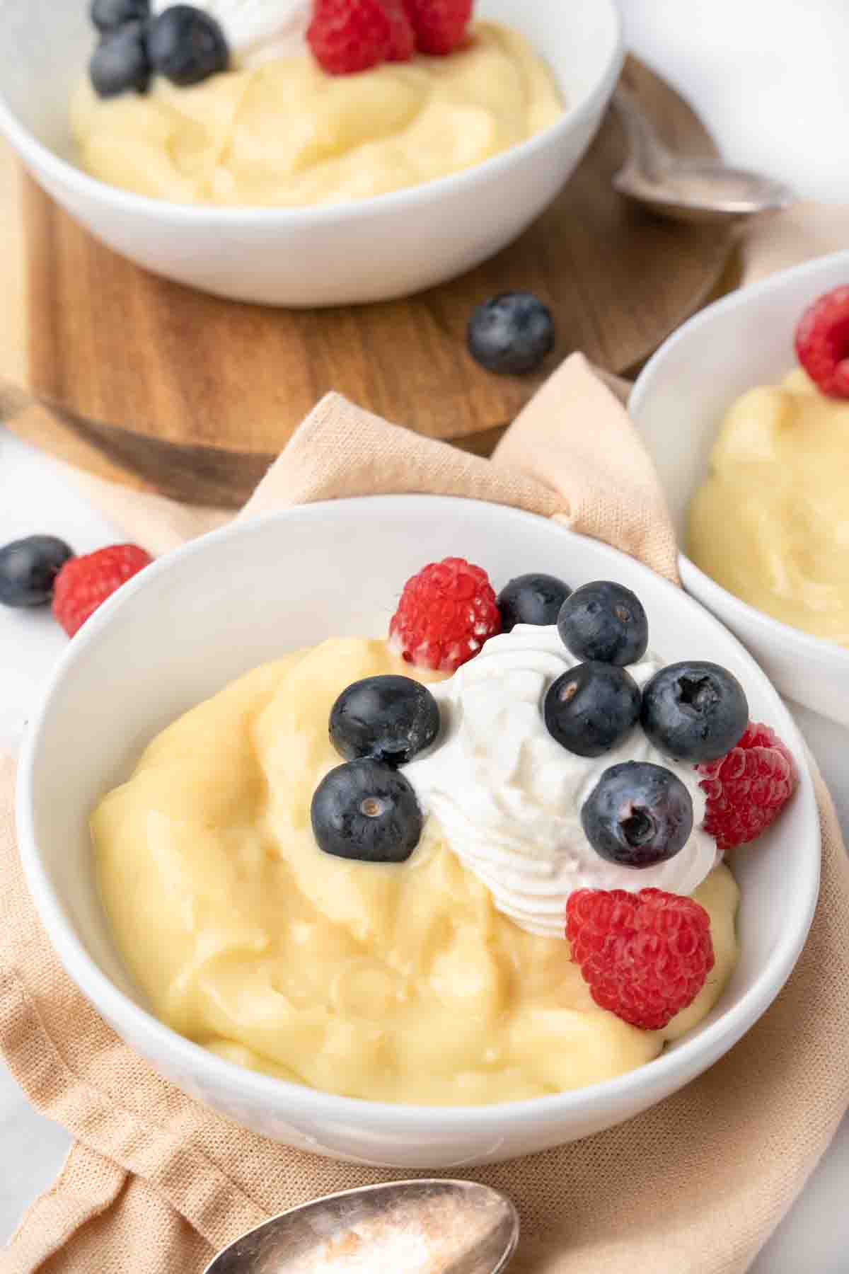 Vanilla custard in a white bowl topped with whipped cream and berries.