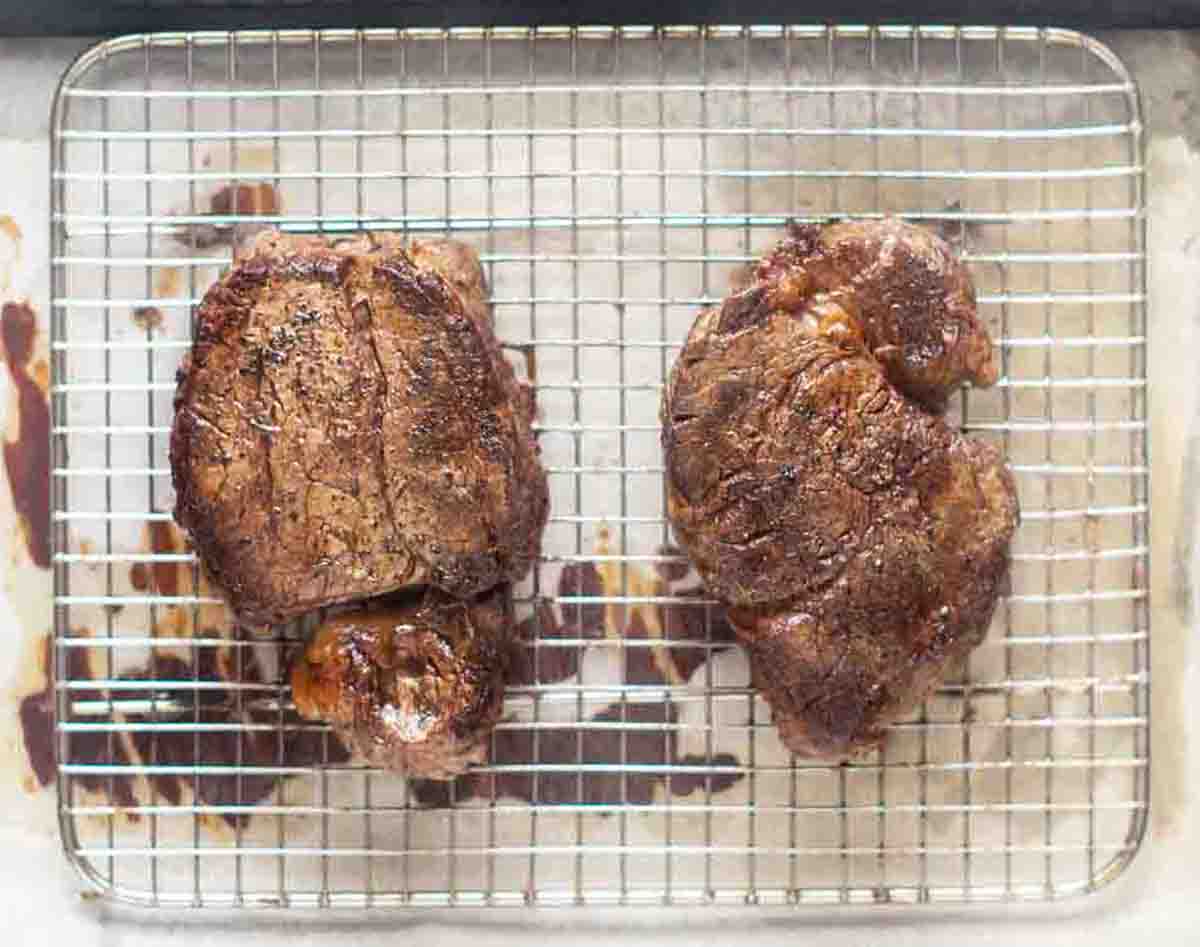 cooked steaks resting on wire rack.