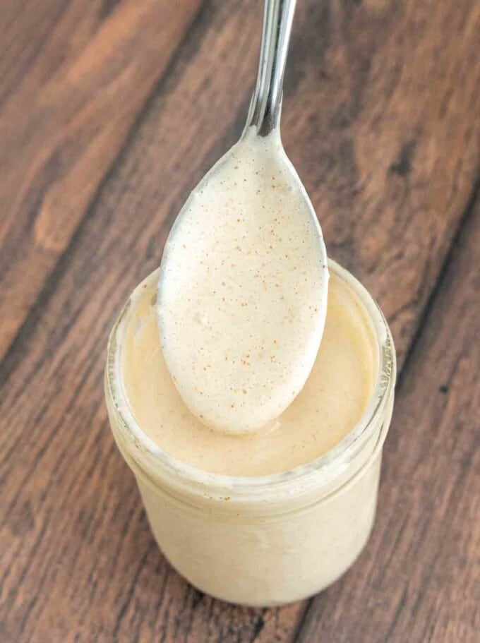 Glass jar of Alabama white sauce with a spoon in it.