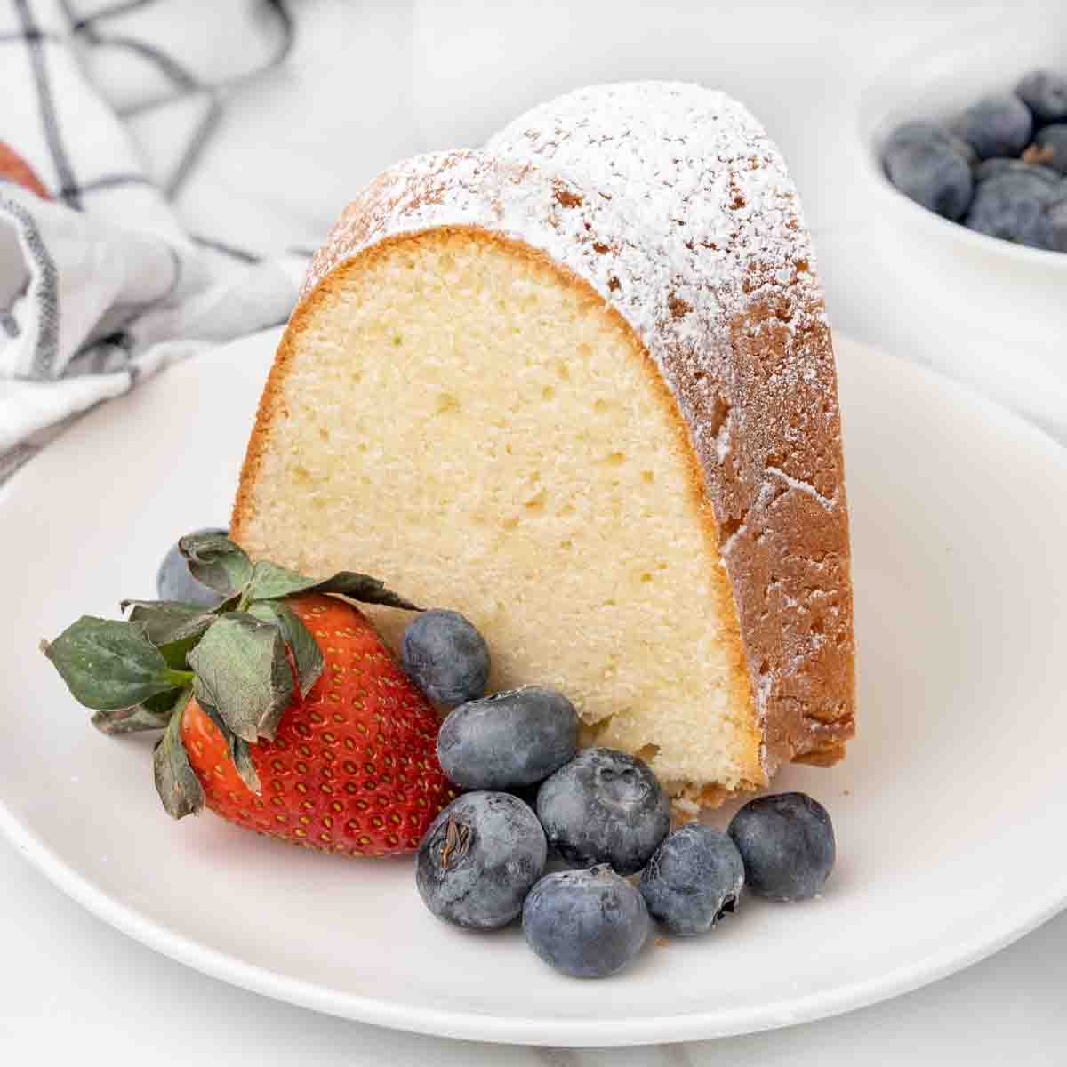 Slice of cream cheese pound cake on white plate with berries.