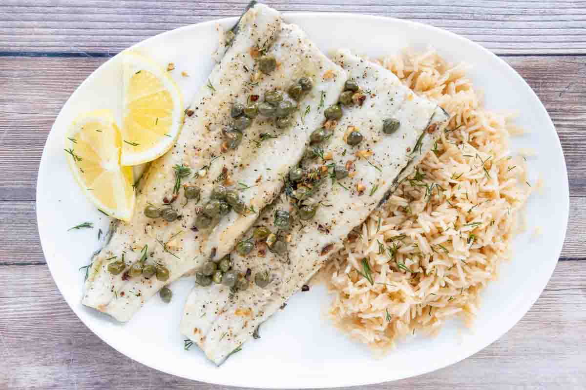 Pan fried rainbow trout with a lemon caper sauce and rice on a white plate.