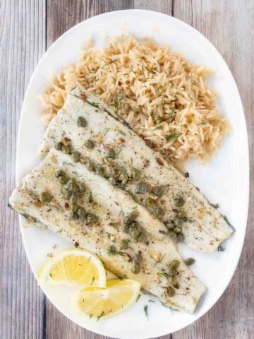 Pan fried rainbow trout with a lemon caper sauce and rice on a white plate.