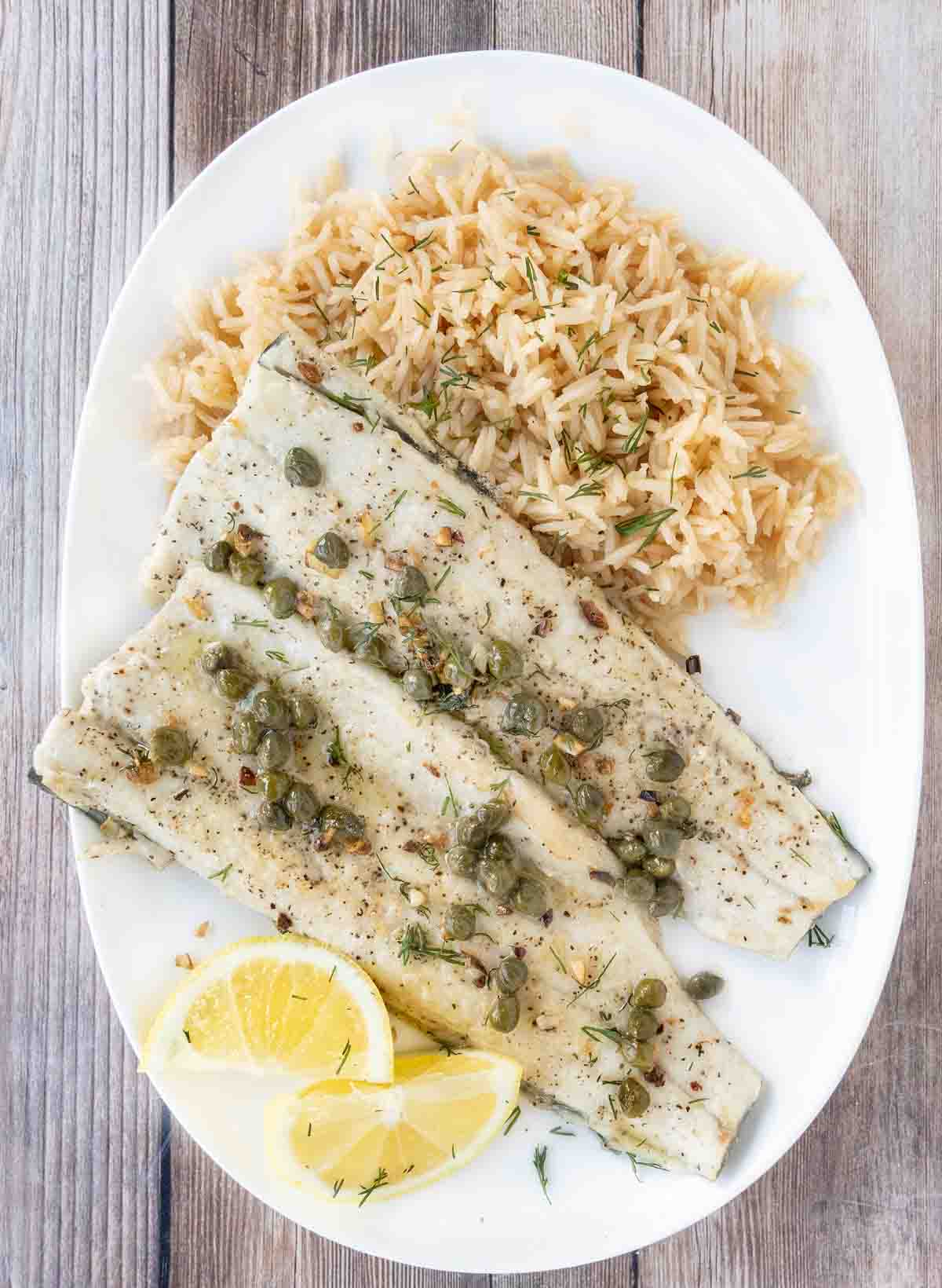 Pan fried rainbow trout with a lemon caper sauce and rice on a white plate.