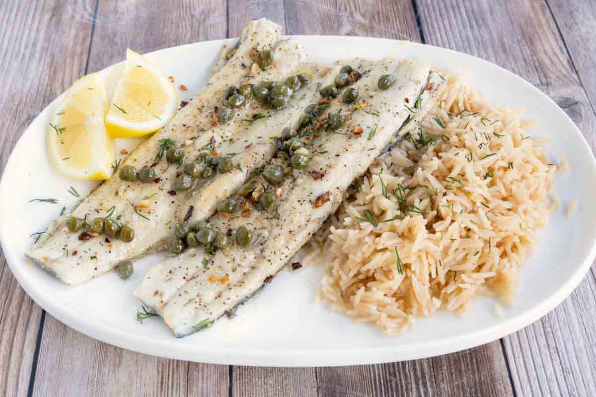 Pan fried rainbow trout with a lemon caper sauce and rice on a white plate.