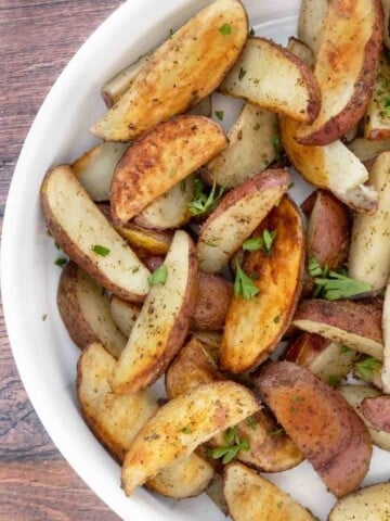 Oven roasted potato wedges in a white bowl.