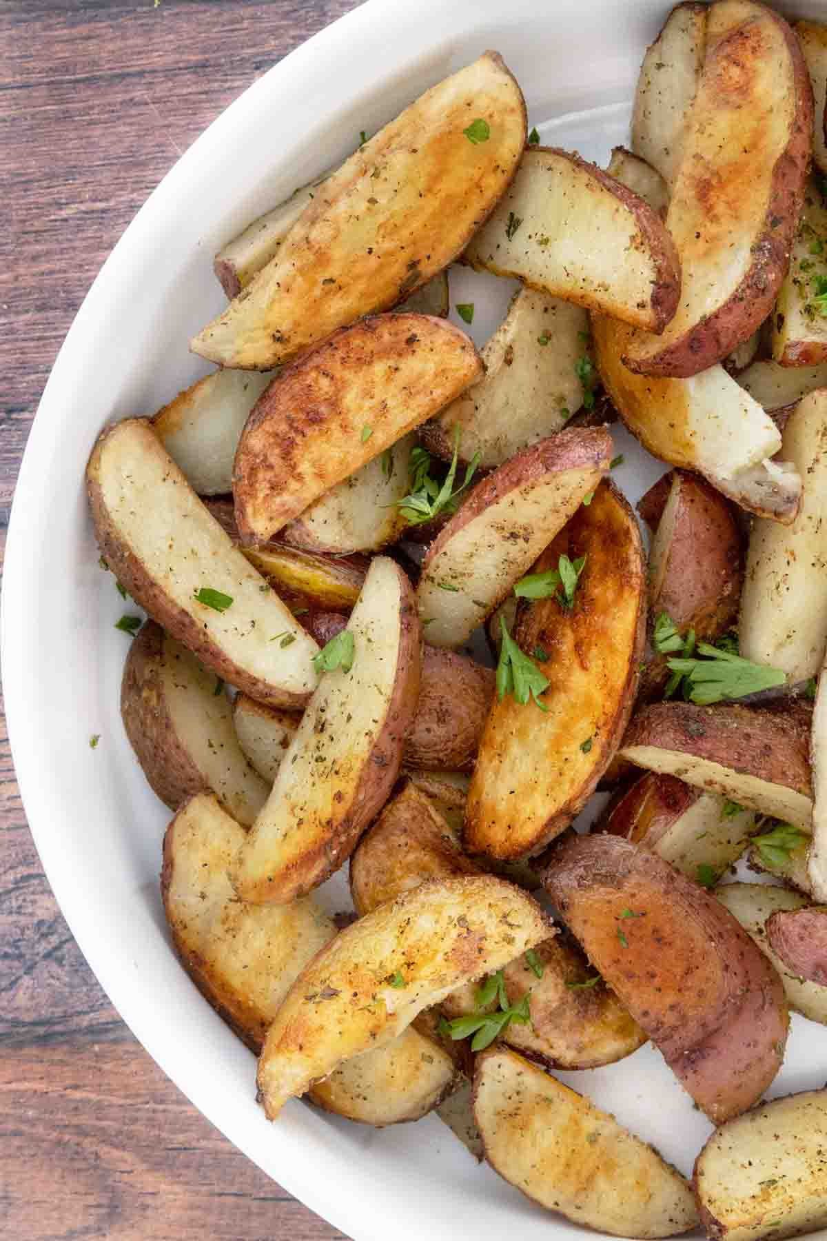 Oven roasted potato wedges in a white bowl.