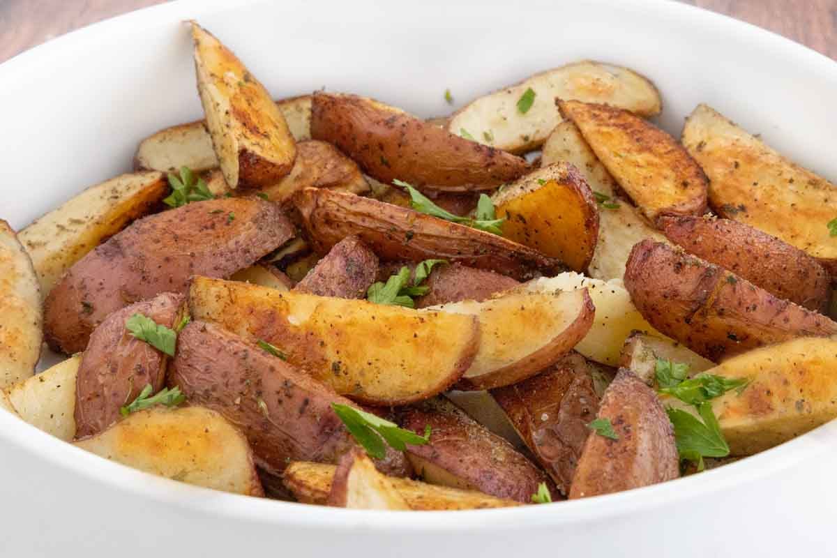 Oven roasted potato wedges in a white bowl.