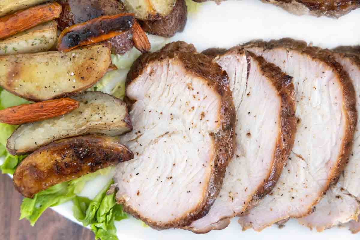 close up of sliced smoked turkey breast with potatoes on a white platter.