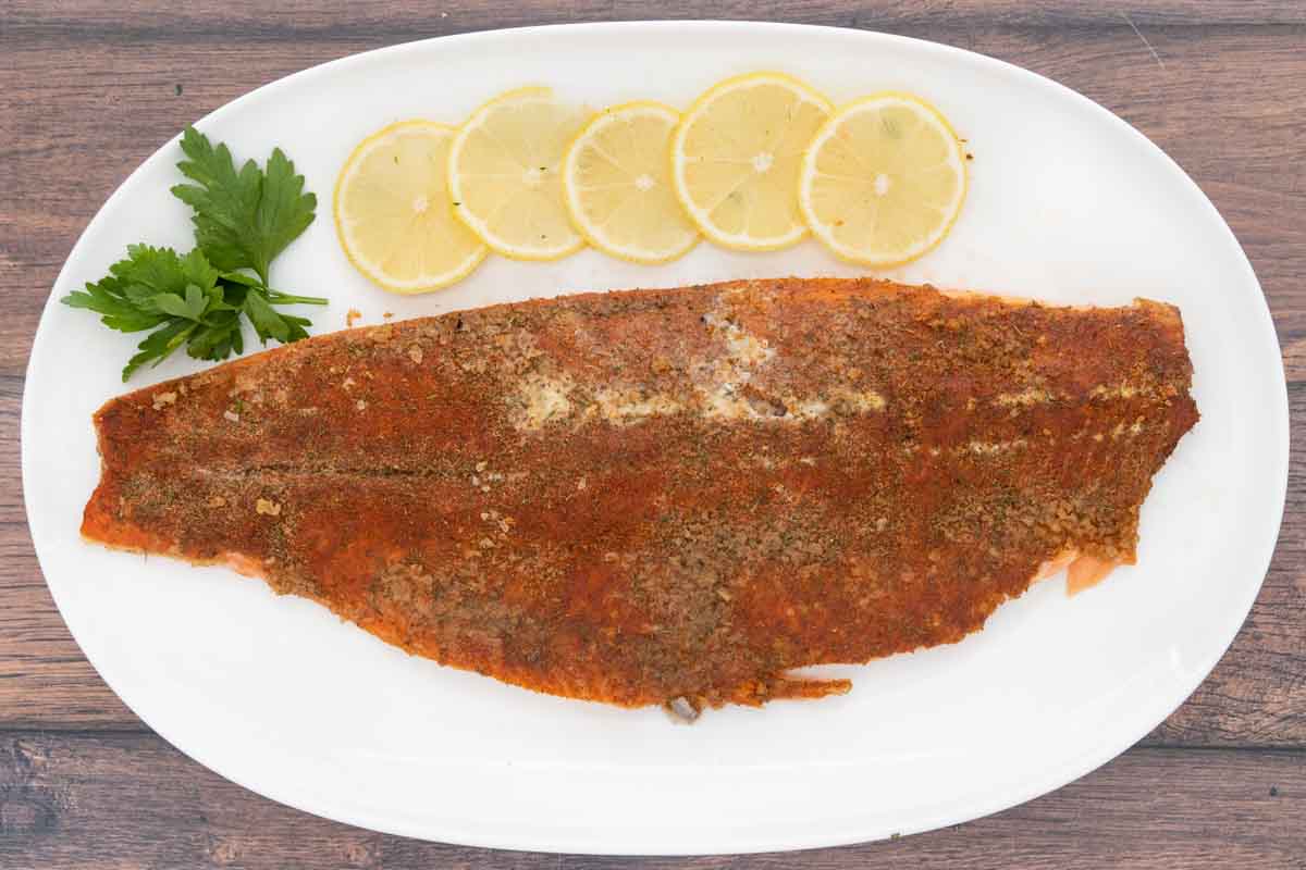 smoked trout on white platter with lemons and parsley.