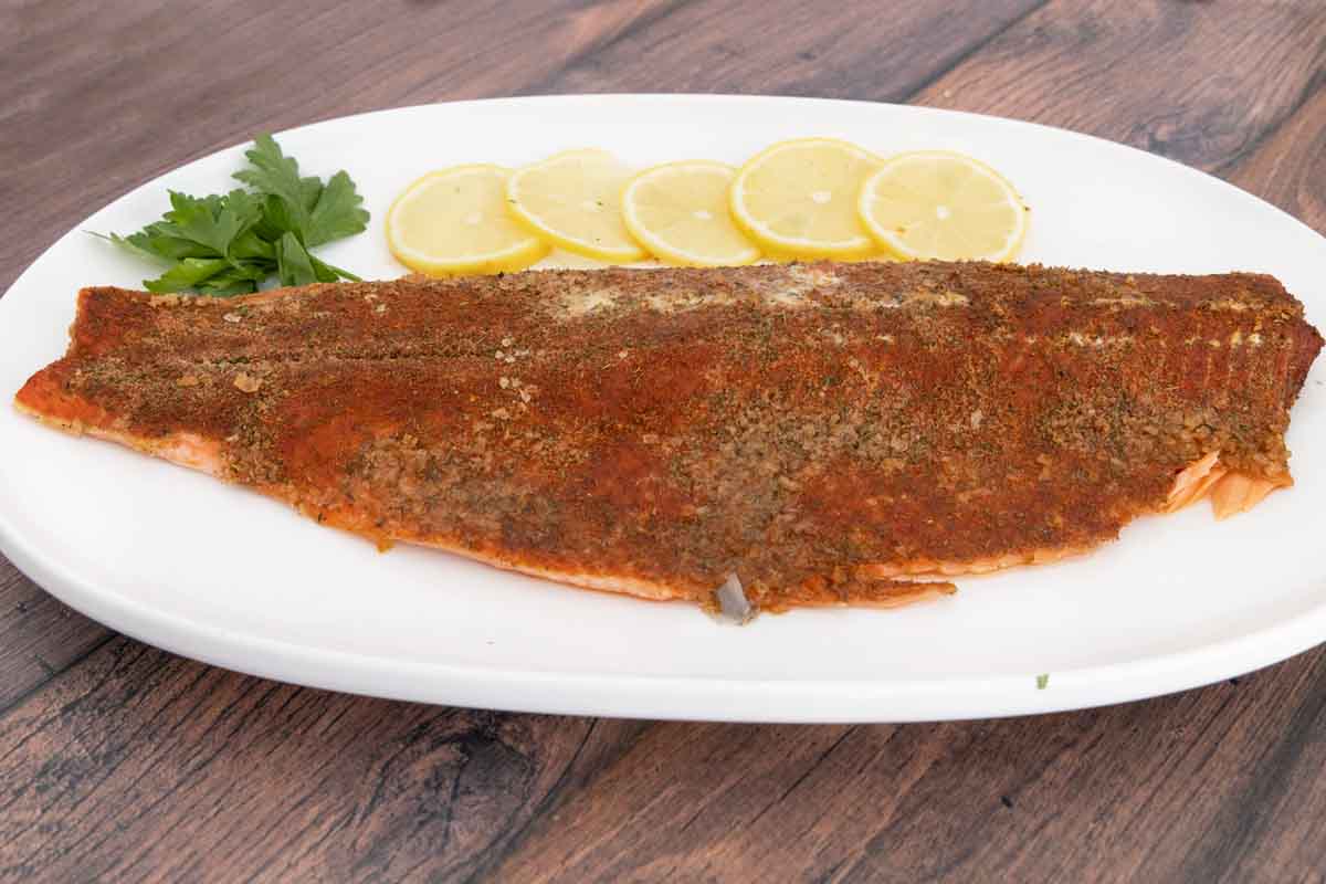 smoked trout on white platter with lemons and parsley.