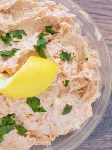 Smoked trout dip in a clear glass bowl with a lemon peel and chopped parsley.