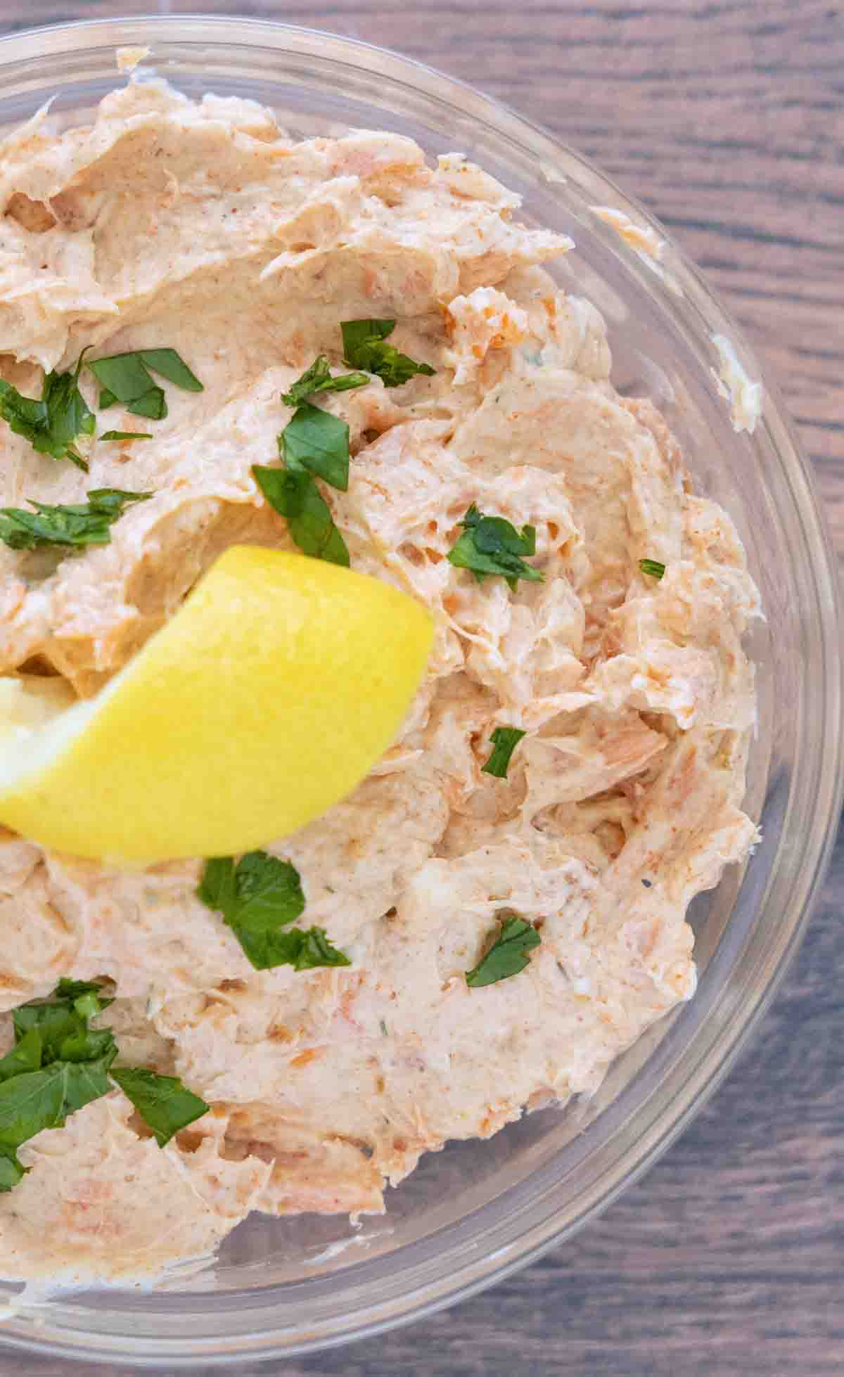 Smoked trout dip in a clear glass bowl with a lemon peel and chopped parsley.