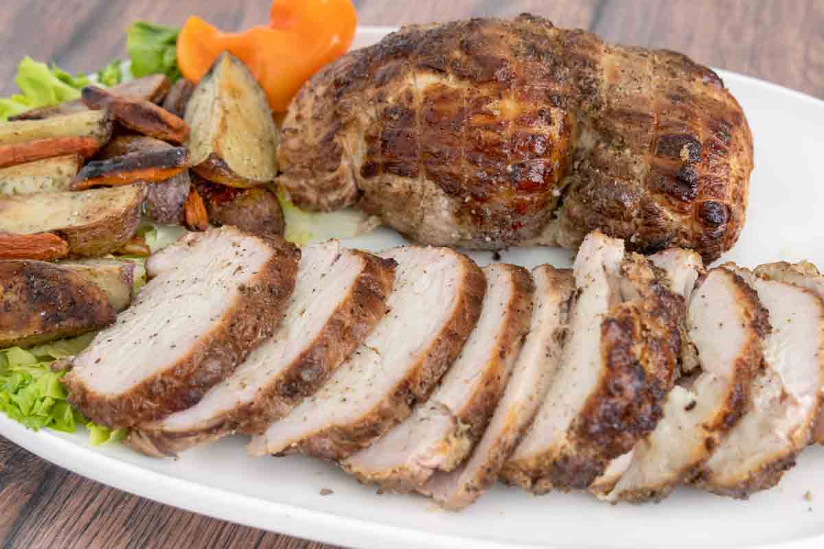sliced smoked turkey breast next to whole smoked turkey breast on a white platter.