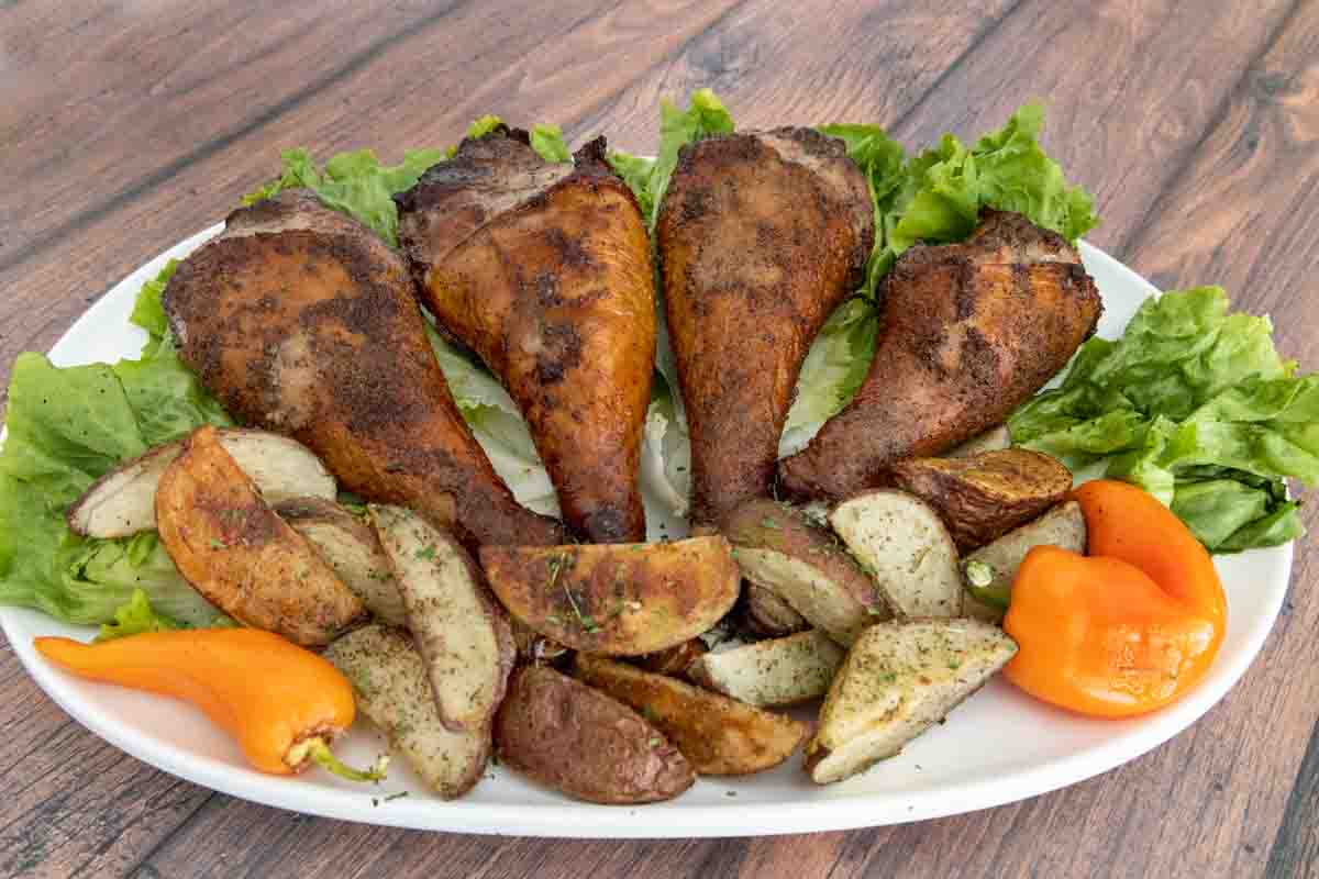 Smoked turkey legs with roasted potatoes on a bed of greens on a white platter.