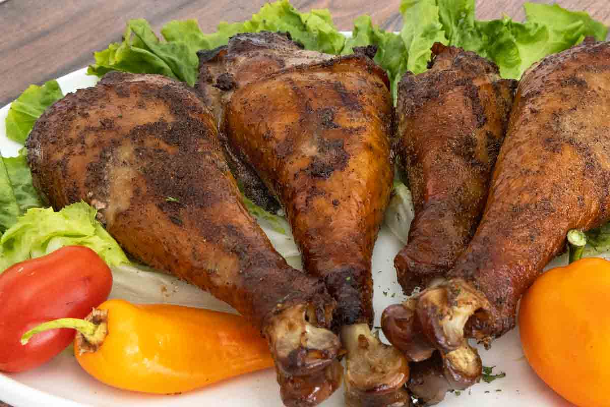 smoked turkey legs on bed of greens on a white platter.