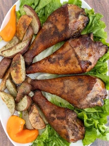 Smoked turkey legs on a bed of greens on a white platter.