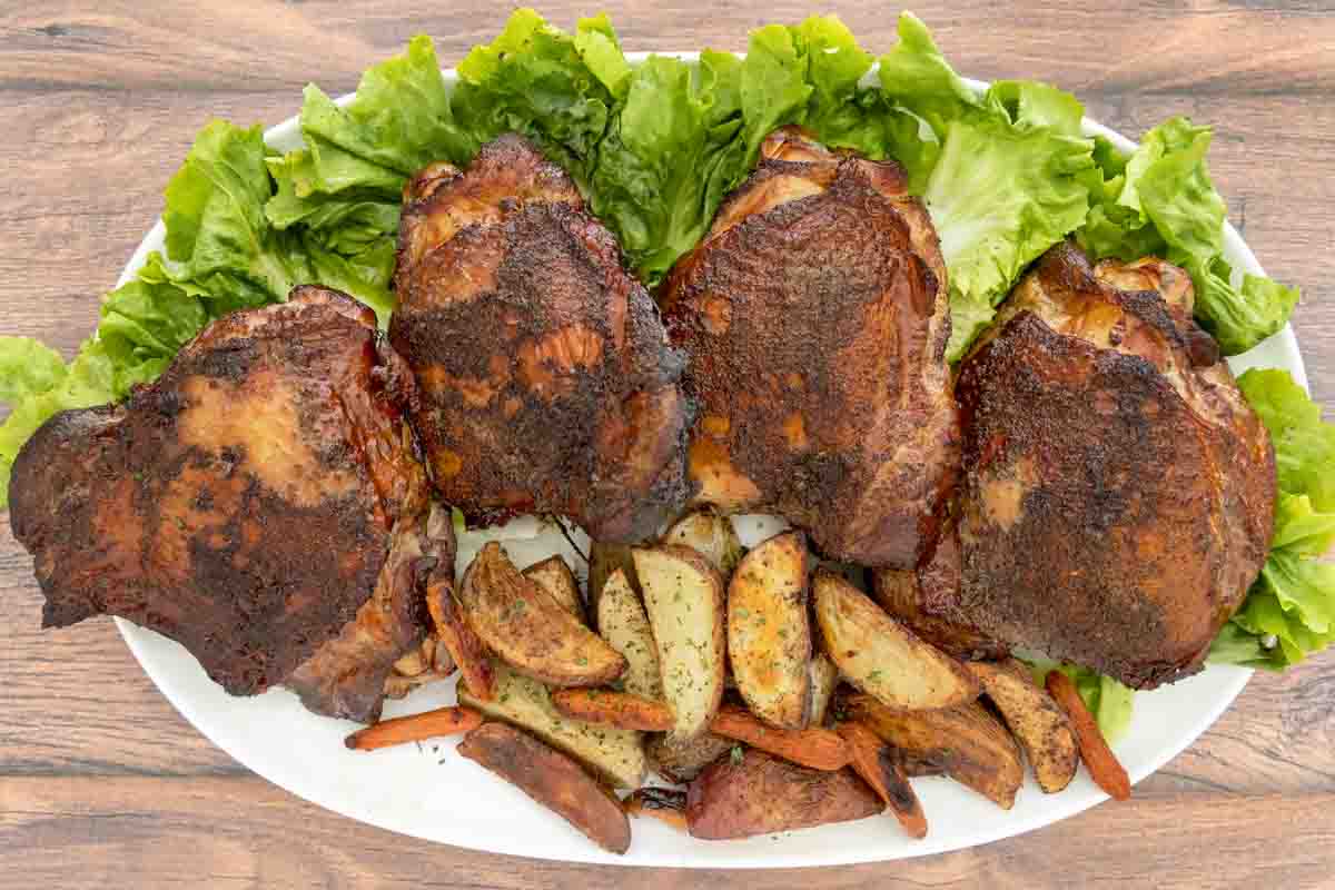 Smoked turkey thighs on a bed of romaine leaves on a white platter with crispy potato wedges.