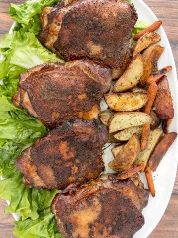 Smoked turkey thighs on a bed of romaine leaves on a white platter with crispy potato wedges.